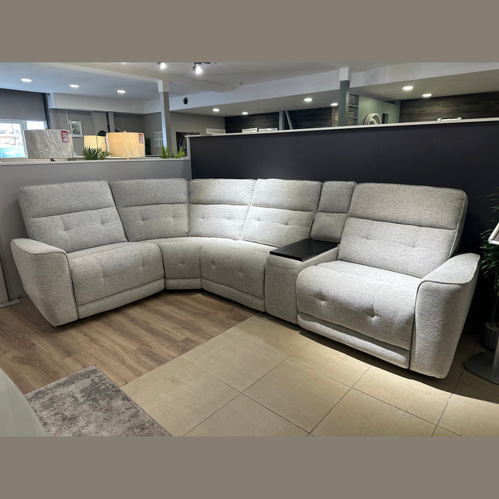 The Avery Electric Recliner Corner, a modern gray L-shaped sectional sofa with tufted backrests and a built-in armrest console in the corner, sits on display atop a mix of tile and wood flooring—making it an ideal centerpiece for any contemporary living room.