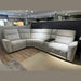 The Avery Electric Recliner Corner, a modern gray L-shaped sectional sofa with tufted backrests and a built-in armrest console in the corner, sits on display atop a mix of tile and wood flooring—making it an ideal centerpiece for any contemporary living room.