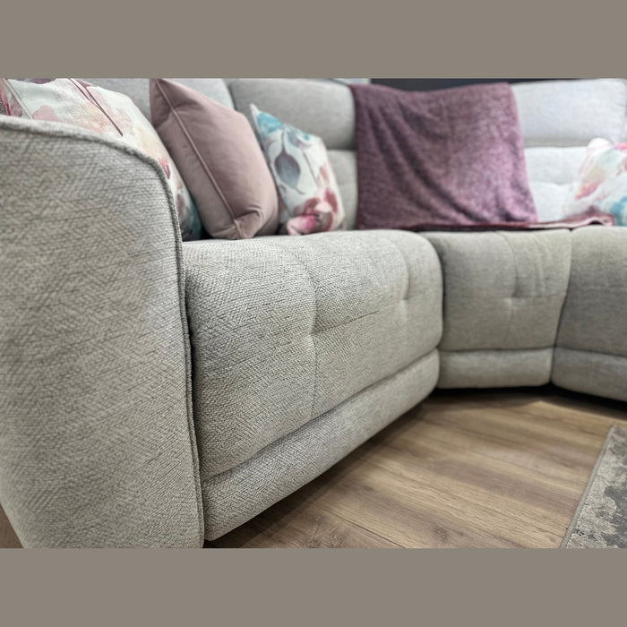 Close-up of the Avery Electric Recliner Corner in light gray fabric, arranged as a sectional and adorned with both floral and plain pillows. A purple throw blanket is draped over the backrest, while the wooden flooring beneath enhances the warmth of the modern living room setting.