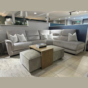 A contemporary living room arrangement showcasing the Lucas Corner, a stylish sofa with washable fabric, accented by white pillows, two gray ottomans, a wooden coffee table, and a Chanel book on a beige rug in the showroom.