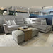 A contemporary living room arrangement showcasing the Lucas Corner, a stylish sofa with washable fabric, accented by white pillows, two gray ottomans, a wooden coffee table, and a Chanel book on a beige rug in the showroom.