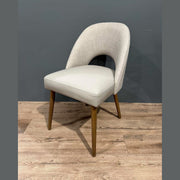 The Florence Dining Chair showcases light gray upholstery, a curved backrest, and wooden legs, set on a light wood floor with a gray wall background.