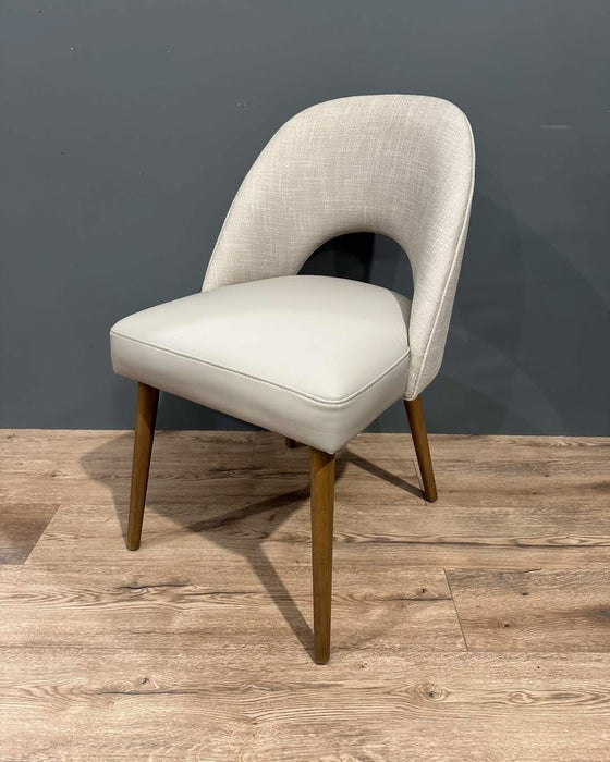 The Florence Dining Chair showcases light gray upholstery, a curved backrest, and wooden legs, set on a light wood floor with a gray wall background.
