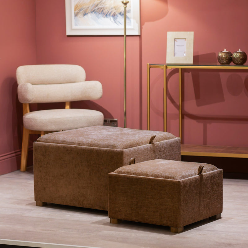 A modern living room with a cream upholstered chair, Maya tray table pouffes - Cappuccino - Set of 2, a gold metal console table with decor, and a tall floor lamp against a pink wall.