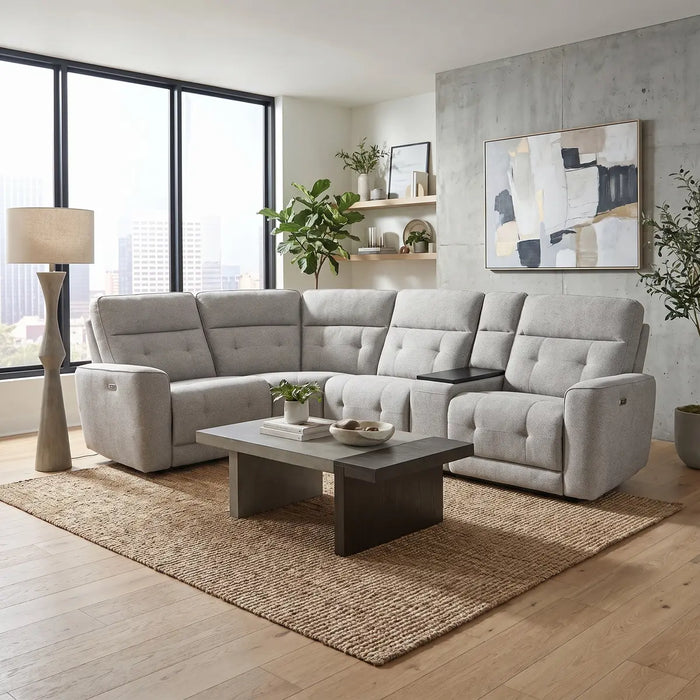 Modern living room with a large light-gray Avery Electric Recliner Corner sofa, rectangular coffee table, floor lamp, plants, abstract wall art, shelves with decor, and large windows with city views. Neutral tones and cozy, minimalist style are complemented by this electric recliner sofa for an enhanced entertainment experience.