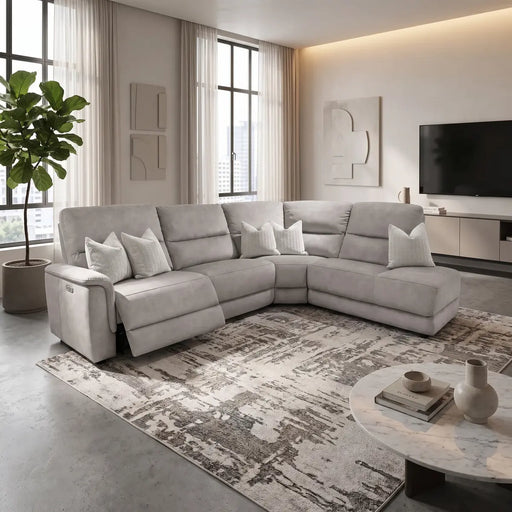 A modern living room featuring the spacious Lucas Corner sofa, designed with easy-care, washable fabric for hassle-free maintenance. The space is accented by a patterned rug, a round marble coffee table, a wall-mounted TV, abstract wall art, and large windows dressed in sheer curtains. A tall potted plant stands in the corner for a touch of greenery.