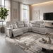 A modern living room featuring the spacious Lucas Corner sofa, designed with easy-care, washable fabric for hassle-free maintenance. The space is accented by a patterned rug, a round marble coffee table, a wall-mounted TV, abstract wall art, and large windows dressed in sheer curtains. A tall potted plant stands in the corner for a touch of greenery.