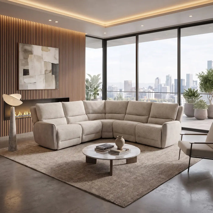 Modern living room showcasing the spacious Willow Corner sofa in beige, featuring easy-clean fabric. The space is complemented by a round coffee table, a stylish armchair, fireplace, abstract art, and floor-to-ceiling windows with city views. Neutral tones and houseplants complete the elegant decor.