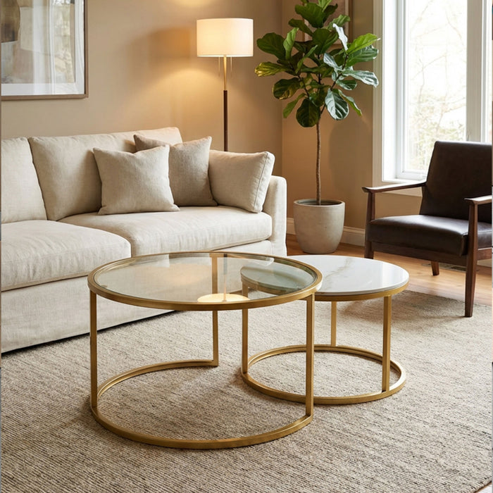 A modern living room featuring the Salzburg Nest, a set of gold-framed marble coffee tables, arranged beside a beige sofa, with a floor lamp, large potted plant, and a dark accent chair by the window atop a textured rug.