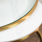 A close-up of the Salzburg Nest’s round tabletop features a white marble surface beneath glass, accented with a gold metal rim and showcasing part of its elegant edge and legs.