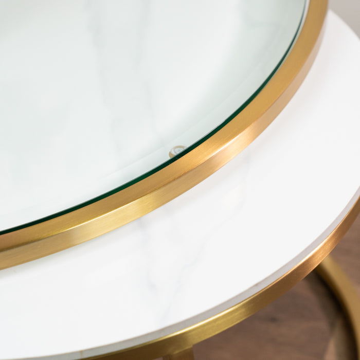 A close-up of the Salzburg Nest’s round tabletop features a white marble surface beneath glass, accented with a gold metal rim and showcasing part of its elegant edge and legs.
