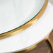 A close-up of the Salzburg Nest’s round tabletop features a white marble surface beneath glass, accented with a gold metal rim and showcasing part of its elegant edge and legs.
