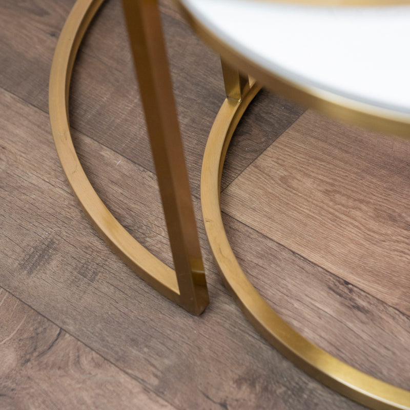 Close-up of a gold metal leg with a circular base from the Salzburg Nest, resting on a wood floor with varying brown tones—an elegant detail often featured in modern coffee tables designed to enhance contemporary living spaces.