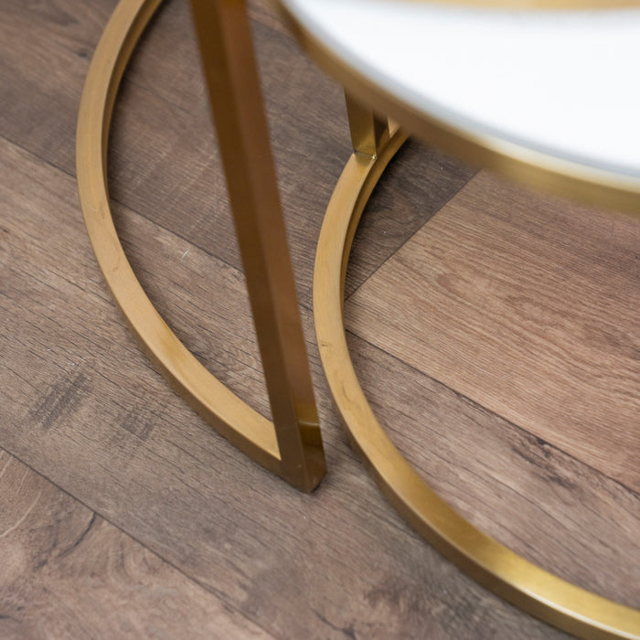 Close-up of a gold metal leg with a circular base from the Salzburg Nest, resting on a wood floor with varying brown tones—an elegant detail often featured in modern coffee tables designed to enhance contemporary living spaces.