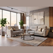Light and spacious modern living room with large windows, featuring a contemporary sofa and the Delta Electric Recliner upholstered in gray easy-clean fabric. The space includes a round glass coffee table, abstract wall art, plants, a floor lamp, wood accents, and offers a cityscape view outside.