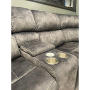The Boston Corner Group is a gray reclining sofa with plush cushions, two built-in cup holders, a center storage compartment, and a wireless charging port. It’s shown sitting against a wall beneath a window ledge.