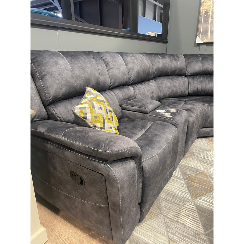 The Boston Corner Group, a gray reclining sectional with wireless charging port and cup holders in the armrest, is set in a modern living room. It features geometric yellow, gray, and white pillows plus a patterned rug against gray walls.