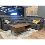 A modern living room with the Boston Corner Group dark gray L-shaped sectional featuring a wireless charging port, yellow and patterned throw pillows, a wooden coffee table, geometric rug, and gold and white tree wall art.