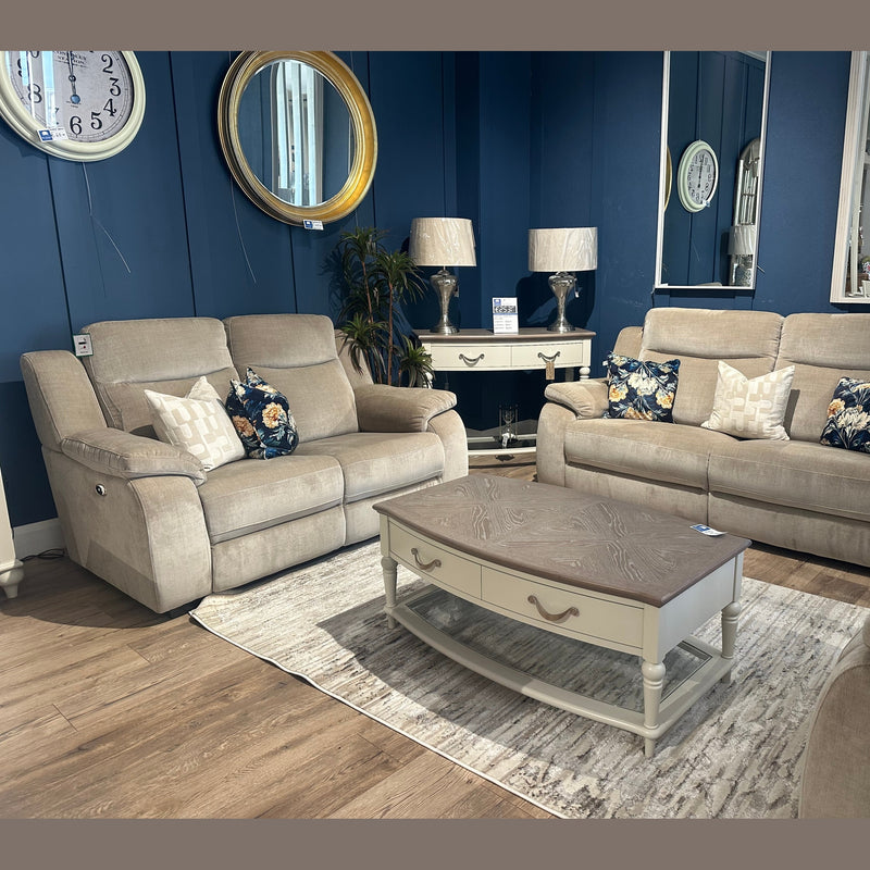 A cozy living room setting features a modern sofa and the Lorenzo Electric Recliner upholstered in taupe washable fabric, paired with two beige sofas adorned with floral and geometric pillows. The space is completed by a wooden coffee table, a side table with lamps, blue walls, wall clocks, mirrors, and warm wood flooring.