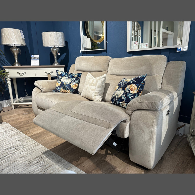 The Lorenzo Electric Recliner, upholstered in modern taupe washable fabric and accented with floral and geometric pillows, is featured in a cozy living room. In the background are two lamps, a white console table, mirrors, and blue walls.