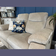 A taupe Lorenzo Electric Recliner with washable fabric and two patterned pillows—one showcasing a blue background adorned with a floral design—sits in a cozy living room with blue walls and decorative lamps in the background, blending modern reclining comfort with inviting style.