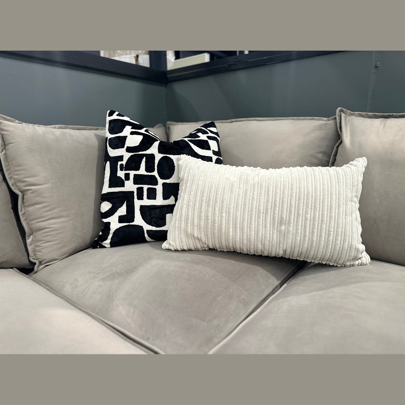A light gray Zoey Chaise Corner sofa featuring a black and white geometric square pillow and a white rectangular corduroy throw pillow.