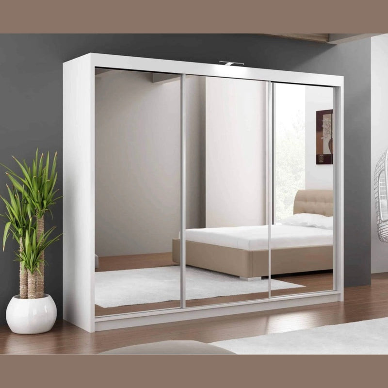 A modern bedroom is highlighted by the Paris 250cm Sliderobe, a large mirrored wardrobe with sliding doors that beautifully reflects a beige bed, white rug, and part of a window. Positioned beside it, a green potted plant adds freshness and style. The elegant Paris 250cm Sliderobe not only maximizes the sense of space but also provides practical bedroom storage solutions.