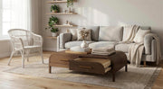 A cozy living room with a light gray sofa, the Sienna Coffee Table, a wicker chair, potted plants on wall shelves, and sunlight streaming through a window onto a woven rug and wooden floor.