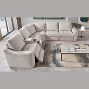 A modern living room features the Velora Corner Group modular sectional in light gray with an electric recliner, paired with a marble coffee table displaying books and decor atop a patterned rug on tiled flooring.