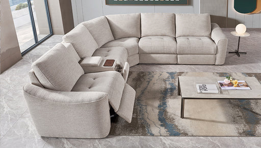 A modern living room features the Velora Corner Group modular sectional in light gray with an electric recliner, paired with a marble coffee table displaying books and decor atop a patterned rug on tiled flooring.