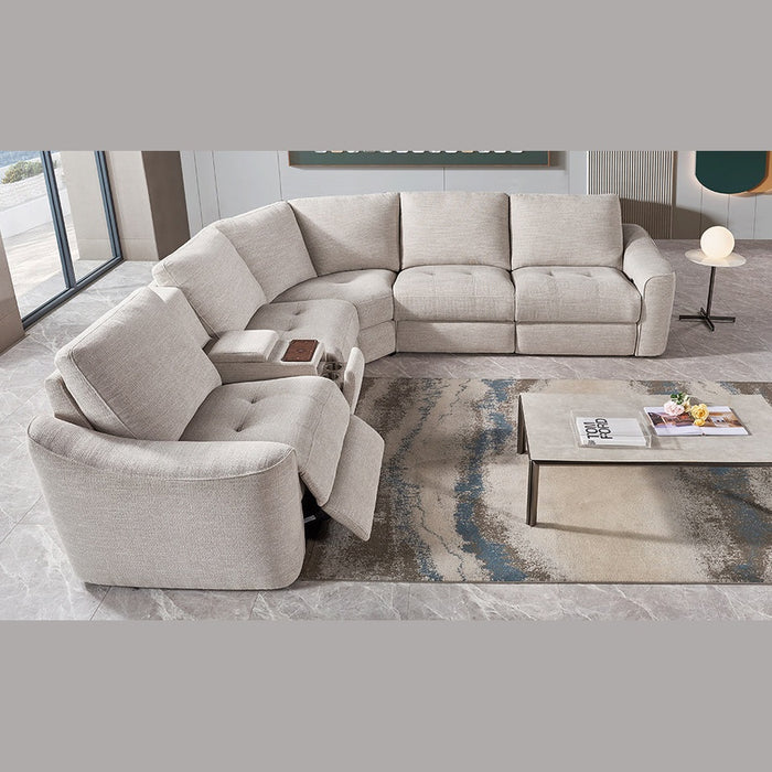 A modern living room features the Velora Corner Group modular sectional in light gray with an electric recliner, paired with a marble coffee table displaying books and decor atop a patterned rug on tiled flooring.