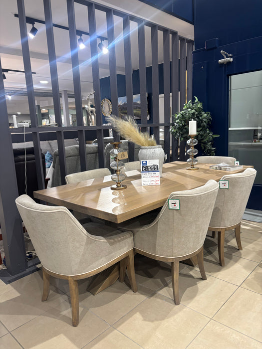 A showroom displays a modern dining set featuring a wooden table and four Louis Dining Chairs in beige upholstery, styled with candlesticks, a clock, dried grass centerpiece, and a visible price tag.