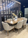 A showroom displays a modern dining set featuring a wooden table and four Louis Dining Chairs in beige upholstery, styled with candlesticks, a clock, dried grass centerpiece, and a visible price tag.