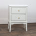 The Monroe 2 Drawer Locker - Stone, a compact white wood accent table with a marble top and round gold drawer knobs, stands on a wood floor against a plain white wall.
