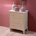 The Monroe Large 3 Drawer Locker - Stone, with yellow knobs, stands against a pink wall. Its white top holds four different ceramic vases. The floor below is light wood.