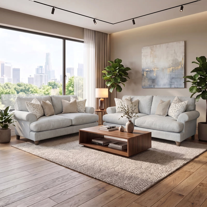 Two light gray Monroe Sofa Range sofas face each other over a wooden coffee table on a textured area rug in a room with a large window overlooking a city skyline.
