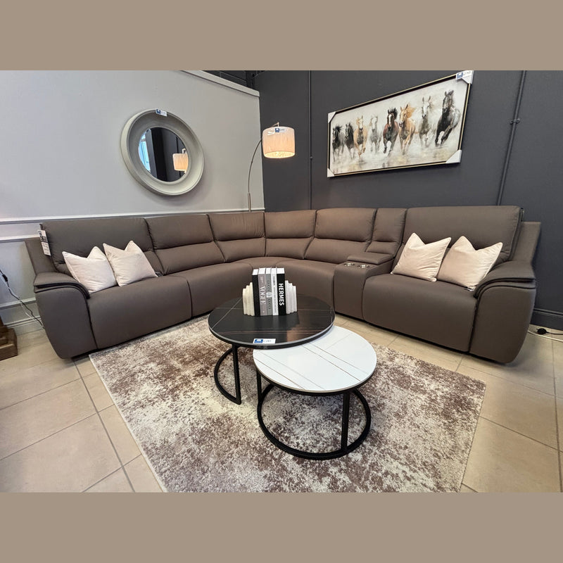 A modern living room features the Vegas Corner Group sofa in gray with beige wipeable pillows, two round coffee tables with books, a beige rug, a floor lamp, a round mirror, and a horse painting on a dark accent wall.