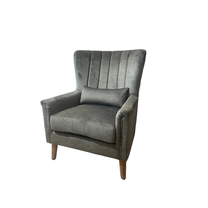 The Charlotte Chair is a comfortable dark gray upholstered accent chair with a high channel-tufted back, wooden legs, and a matching lumbar cushion, shown against a plain white background.