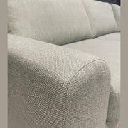 Close-up of the Harold Chaise Corner, a light gray mid-century sofa with a textured fabric surface, displaying the armrest, seat cushions, and backrest against a dark wall background.