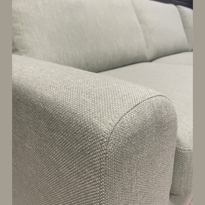 Close-up of the Harold Chaise Corner, a light gray mid-century sofa with a textured fabric surface, displaying the armrest, seat cushions, and backrest against a dark wall background.
