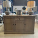 A Marlo Sideboard in American oak, topped with two lamps and three books, stands in a modern showroom featuring mirrors, tables, chairs, and hanging white paper lanterns in the background.