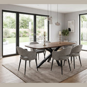 A New York Dining table & 6 Macey Chairs featuring a rectangular top and black x-shaped base, surrounded by six upholstered chairs with tapered metal legs, set on a large area rug in a sunlit room.