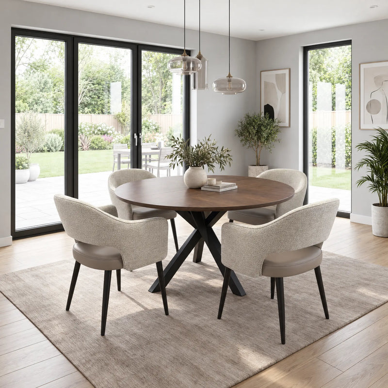 The New York Round Table is a walnut extending dining table with a round top and black crisscross base, surrounded by four upholstered chairs with curved backs.