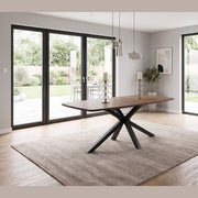 A New York Dining table & 6 Macey Chairs with a black geometric metal base, set on a large rug in a bright room with sliding glass doors.