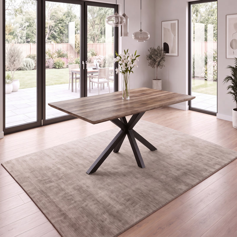 Elson 1.6 Dining Table with a dark wood-grain top and a black geometric metal base with X legs, set on a rug in a bright room.