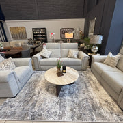A modern living room showroom features the Luna Electric Recliner, styled with patterned pillows, a round marble coffee table, a decorative rug, and home decor accents, all set amidst large windows and dark accent walls.