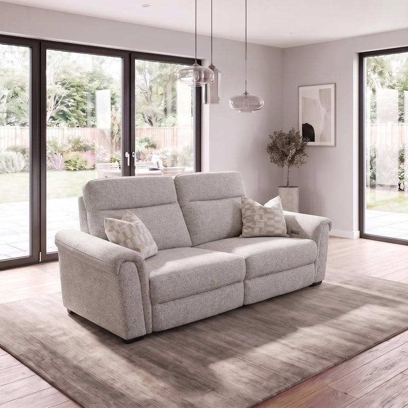 Luna Electric Recliner in light gray fabric, a two-seater sofa with two patterned throw pillows, centered on a rug in a sunlit living room.