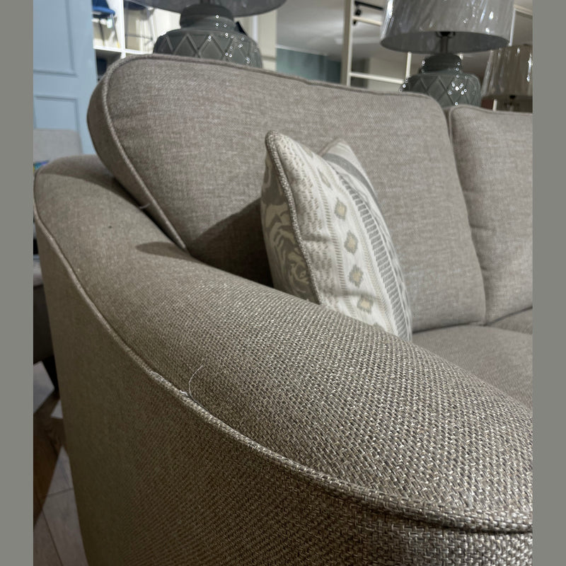 The Shelly sofa by vendor-unknown is a beige modern design in aquaclean fabric, shown close-up with a patterned cushion on a wooden floor, near grey lamps and decorative shelves in the background.