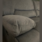Close-up of the Gibson Electric Recliner, a 3-seater gray upholstered sofa with plush armrests and backrests, set against a dark green wall. The grey washable fabric texture is visible, with a round mirror partly seen at the top right corner.