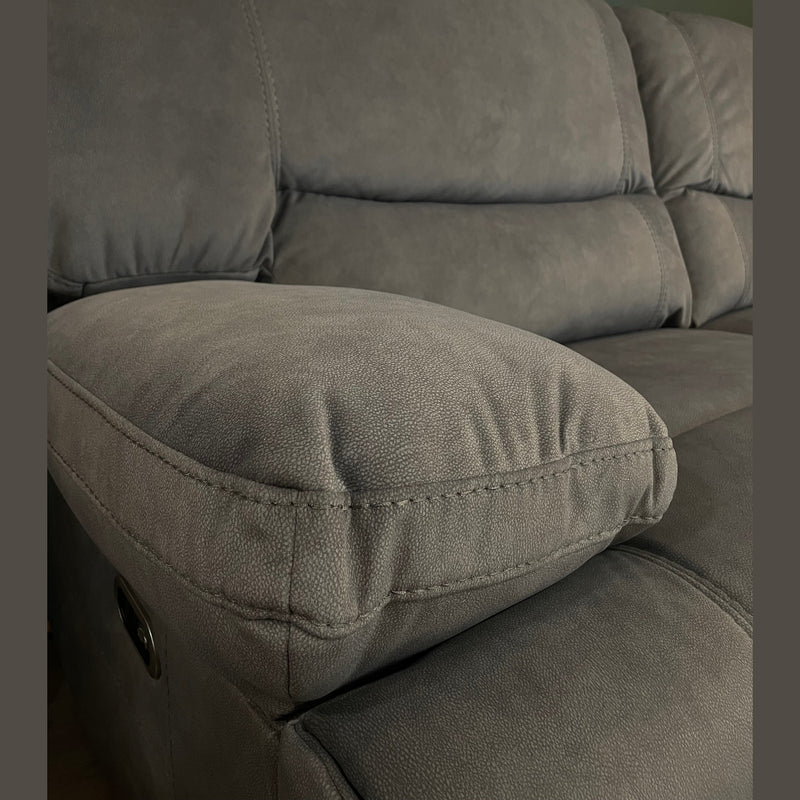 Close-up of the Gibson Electric Recliner, a 3-seater gray upholstered sofa with plush armrests and backrests, set against a dark green wall. The grey washable fabric texture is visible, with a round mirror partly seen at the top right corner.